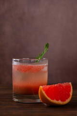 Fresh cocktail with grapefruit, peach, rosemary, ice and a slice of grapefruit on a brown table. Vertical orientation.