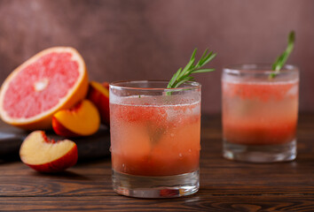 Grapefruit and peach lemonade with rosemary and ice on a wooden brown background. Healthy drink, sugar and alcohol free.