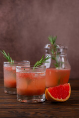 Grapefruit drink lemonade with rosemary and peach in a glasses with a slice of grapefruit on a brown wooden table. Healthy drink, sugar and alcohol free. Vertical orientation.