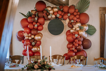 A festive balloon arch in red and gold with floral accents surrounds a blank circular sign, set...