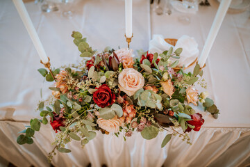 A close-up of a floral centerpiece with roses, greenery, and candles on a white tablecloth, creating an elegant and romantic table setting.