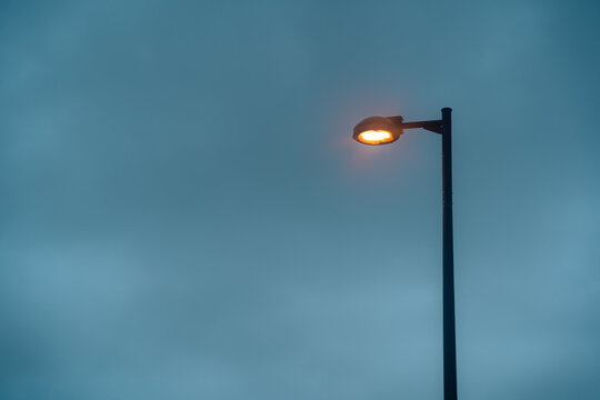 Modern street lamp is turning on with orange light, isolated by dark cloudy sky. Took during summer season in Naha, Okinawa, Japan. Perfect for graphic resource, background or wallpaper