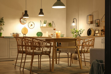 Interior of modern kitchen with glowing lamps, white counters, chairs and dining table at evening