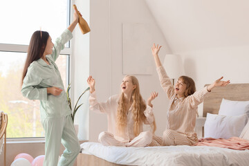 Happy young woman with bottle of champagne and her bridesmaids at Hen Party in bedroom