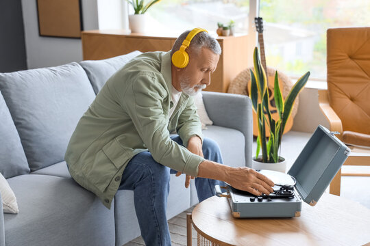 Mature man in headphones with record player listening to music on sofa at home