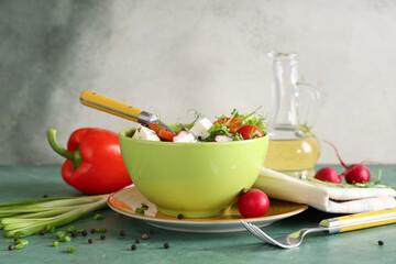 Bowl of fresh vegetable salad with radish and feta cheese on green table