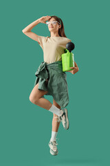 Female gardener with watering can jumping on green background