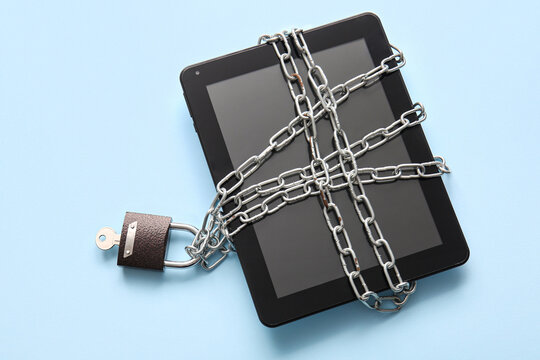 Modern tablet computer tied with chain and padlock on color background
