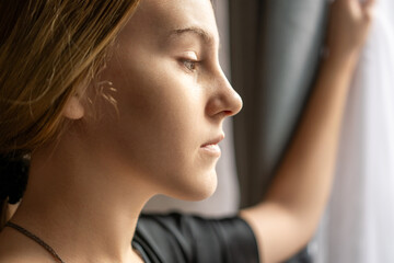 Woman Window Sadness Contemplation: Young woman by window, pensive expression, indoor setting, emotional reflection.