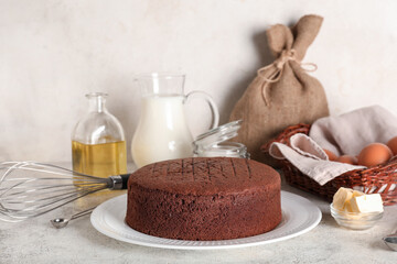 Delicious chocolate sponge cake with ingredients and whisk on light grunge background