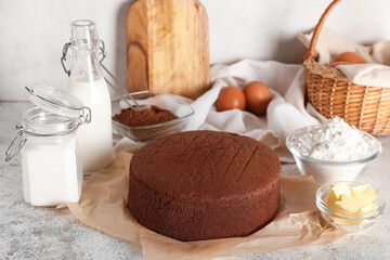 Tasty chocolate sponge cake with ingredients on light grunge background