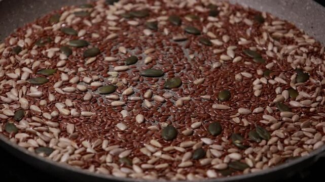 Close-up video of a mix of sunflower, pumpkin, and flax seeds being cooked in a pan, showcasing a healthy and nutritious ingredient preparation