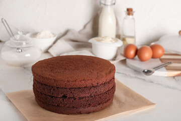 Delicious chocolate sponge cake cut into layers with ingredients on light background