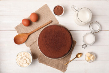 Delicious chocolate sponge cake with ingredients on white wooden background