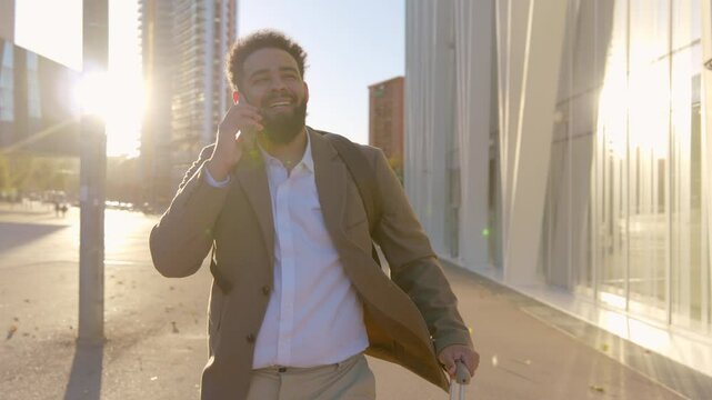 Accomplished African American businessman confidently stands on bustling city on a call, surrounded by skyscrapers and vibrant energy, reflecting his success in the warm sunlight and stron wind