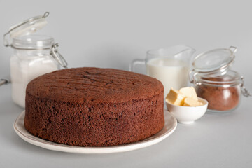 Delicious chocolate sponge cake with ingredients on grey background