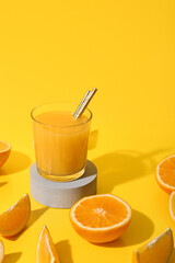 Decorative podium with glass of fresh orange juice and cut fruits on yellow background