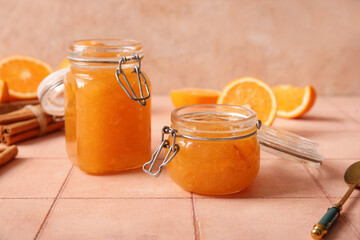 Jars of sweet orange jam with cinnamon and fruits on beige tile table