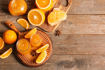 Jars of sweet orange jam with star anise and slices of bread on wooden background