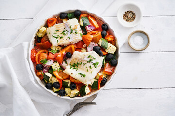 A vibrant dish featuring pieces of fish atop a colorful arrangement of fresh vegetables including tomatoes, zucchini, and bell peppers, garnished with herbs