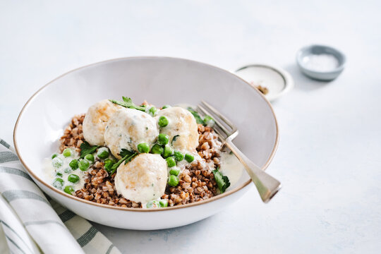 A nourishing bowl features turkey meatballs over a base of cooked grains and vibrant green peas, garnished with herbs, ready for a satisfying meal any time of day