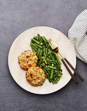 This visually appealing dish features two salmon cakes placed on a plate, accompanied by fresh green beans garnished with nuts. The setup emphasizes a healthy and satisfying meal