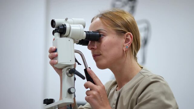 Female medic in grey uniform sets the colposcopy equipment. Gynecology examination in female hospital.
