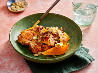 Juicy pieces of roasted chicken are paired with roasted pumpkin and topped with crunchy nuts. The dish is presented in a rustic bowl, highlighting a cozy dining experience