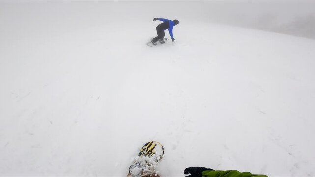 Footage of a person catching up with his fellow sportsman riding ahead. Snowboarding on the snowy day in the mountains.