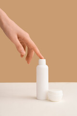 Female hand with bottle and jar of cosmetic products on beige background