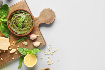 Wooden board with bowl of delicious pesto sauce and ingredients on white background