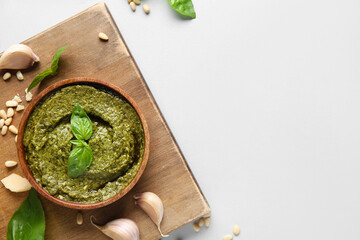Wooden board with bowl of delicious pesto sauce, garlic, pine nuts and basil leaves on white...