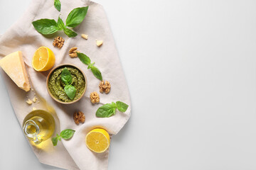 Bowl of delicious pesto sauce with ingredients and jug of oil on white background