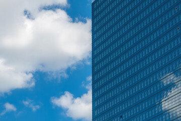 Fototapeta premium Modern glass building reflects clouds in a clear blue sky during a sunny day in an urban environment