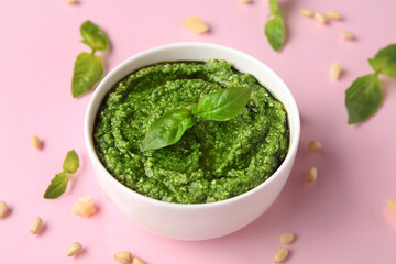Bowl of delicious pesto sauce with basil leaves, pine nuts and cheese on pink background