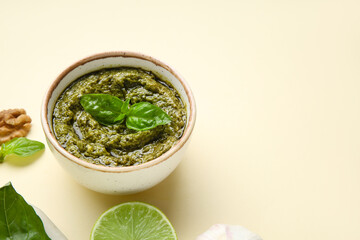 Bowl with delicious pesto sauce and basil leaves on beige background