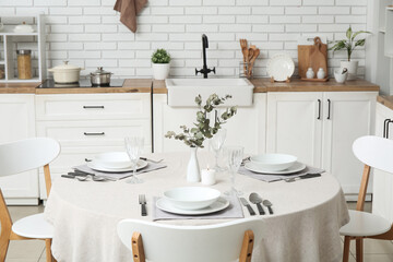Minimalist table setting with white tablecloth, plates, glasses, cutlery and vase in dining room