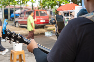Street musicians or buskers singing using guitars and smartphones to memorize song lyrics, creating...