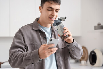 Handsome young man with bottle of water and mobile phone at home