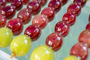 Close-up of glossy candied grapes on skewers, featuring vibrant red and green colors with a shiny...