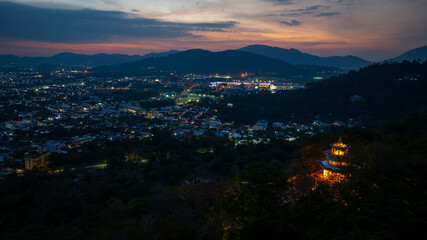 Aerial view of scenery Khao Rang viewpoint at twilight..view of a town nestled among lush green mountains at sunset, with a Pavilion structure perched on the hillside at Phuket town at Dusk