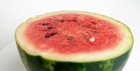 A slice of watermelon is shown on a white background. The watermelon is cut in half, revealing its juicy red flesh. Concept of freshness and summertime.