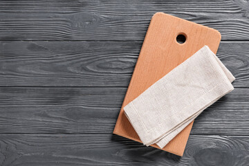 Cutting board with napkin on black wooden table, top view