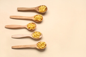 Wooden spoons with raw pasta shells on beige background