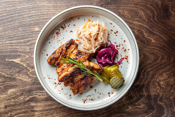 Grilled meat served on a stylish plate, accompanied by pickled vegetables, sauerkraut, and fresh herbs. A flavorful dish perfect for food lovers and culinary presentations.