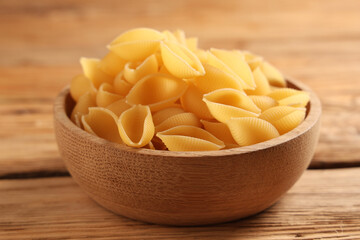 Bowl with raw pasta shells on wooden background, closeup