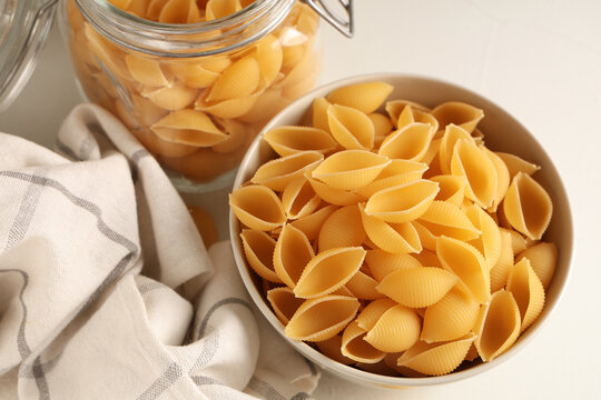 Bowl and jar with raw pasta shells on white background, closeup