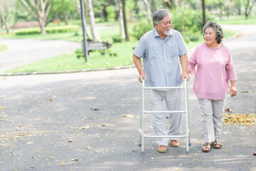 Happy in love Asian senior couple walking in the park. Senior man using walker
