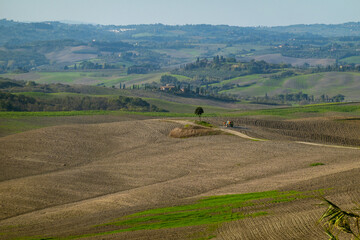 Fototapeta premium Sprawling rural scenery featuring open fields, a lone tree, distant farm buildings, and a vehicle.