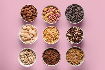 Bowls with different cornflakes on pink background